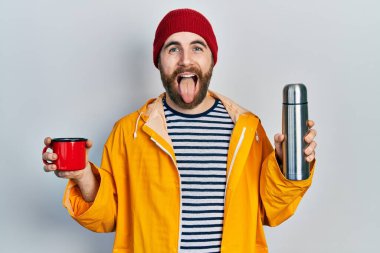 Beyaz, sakallı, elinde kahve fincanı ve termosu olan, komik bir ifadeyle dilini dışarı çıkaran bir adam.. 