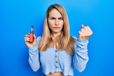 Elektronik sigara tutan beyaz bir kadın öfkeyle bağırıyor, öfkeyle bağırıyor ve el kaldırıyor. 