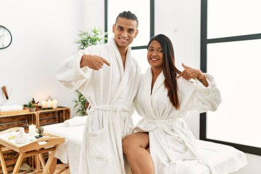 Havlu giymiş genç Latin bir çift güzellik merkezinde duruyor. Kendine güvenen, gülümseyen, kendini gururlu ve mutlu gösteren bir çift.. 