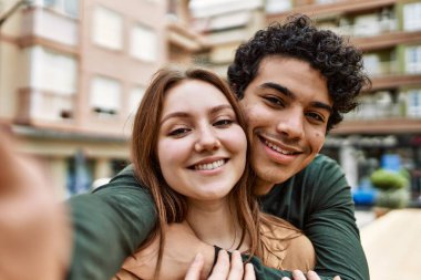 Mutlu bir şekilde gülümseyen ve kucaklaşan genç bir çift kentteki kameranın önünde selfie çekiyor..