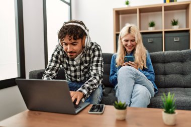 Evde dizüstü bilgisayar ve akıllı telefon kullanan genç çift mutlu..