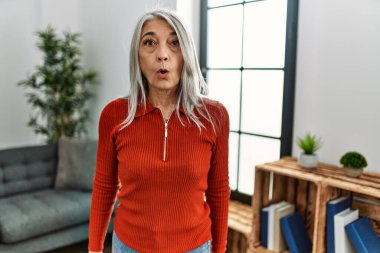 Orta yaşlı, gri saçlı, sıradan kıyafetler giyen bir kadın evde korkmuş ve ağzı açık bir şekilde şaşkınlık içinde, inançsız bir yüz ifadesi takındı. 