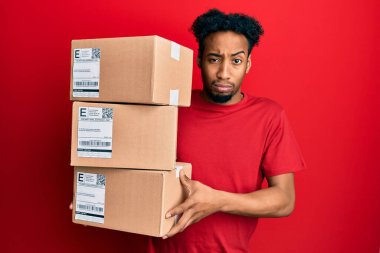 Sakallı genç Afro-Amerikan bir adam teslimat paketlerini kuşkucu ve gergin tutuyor, sorun yüzünden surat asıyor. negatif kişi. 