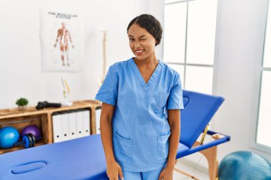 Güzel İspanyol fizyoterapist kadın ağrı kesici kliniğinde kameraya seksi bir ifadeyle bakıyor, neşeli ve mutlu bir yüzle.. 