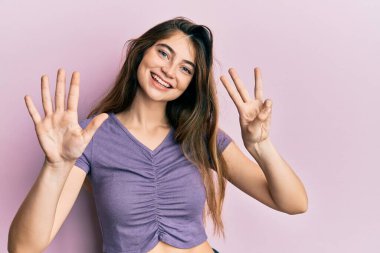 Gündelik giysiler giyen genç beyaz kadın sekiz numarayı gösterip işaret ederken kendinden emin ve mutlu bir şekilde gülümsüyor.. 