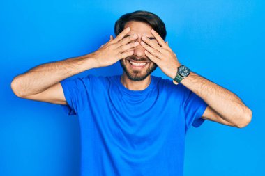 Latin asıllı genç adam günlük kıyafetler giyiyor. Gözleri kapatıyordu. Neşeli ve komik gülümsüyordu. kör kavram. 