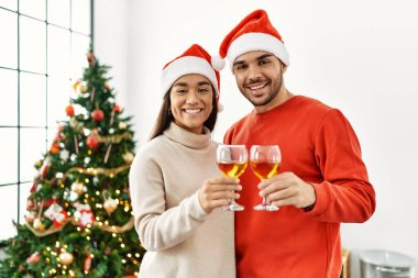 Genç İspanyol çift mutlu bir şekilde kadeh kaldırırken evde Noel ağacının yanında duruyor..