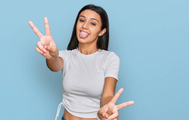 Latin asıllı genç bir kız, günlük beyaz tişörtler giyip iki elini de göstererek gülümseyerek zafer işareti yapıyor. İki numara.. 