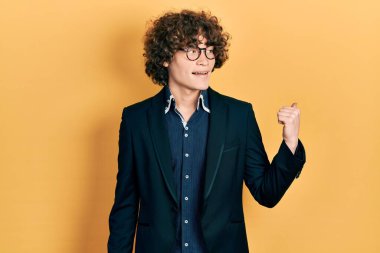 İş ceketi ve gözlük takan yakışıklı genç adam mutlu yüzle gülümsüyor ve başparmağıyla yan tarafı işaret ediyor.. 