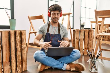 Genç İspanyol ressam, sanat stüdyosunda kulaklık ve dizüstü bilgisayar kullanarak video görüşmesi yapıyor..