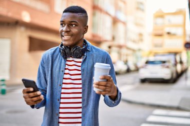 Genç Afrikalı Amerikalı adam akıllı telefon kullanıyor. Şehirde kahve içiyor..