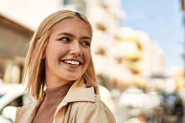 Genç sarışın kız gülümsüyor, mutlu bir şekilde şehirde duruyor..