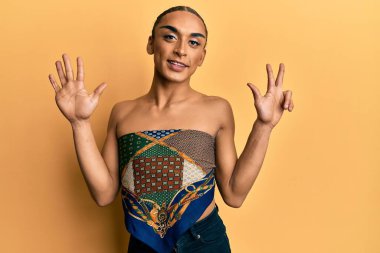 Makyaj yapan, uzun saçlı, kadın bluzu giyen İspanyol bir adam 8 numaralı parmaklarıyla kendini beğenmiş ve mutlu gülümserken kendini gösteriyor.. 