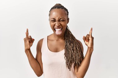 Saçları örgülü siyah bir kadın izole edilmiş arka planda duruyor çılgın bir ifadeyle el kaldırarak rock sembolü yapıyor. Müzik yıldızı. ağır kavram. 