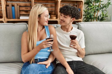 Genç çift mutlu bir şekilde kadeh kaldırıyor kırmızı şarap kadehiyle evde..