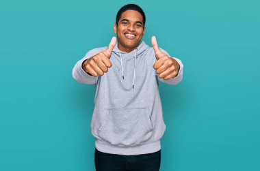 Genç, Latin asıllı, sıradan bir tişört giyen, elinde olumlu bir jest yapmayı onaylayan, gülümseyen ve başarı için mutlu genç bir adam. kazanan jest. 