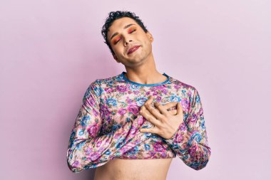 Makyaj yapan yakışıklı bir adam. Moda kıyafetleri giyiyor. Elleri göğsünde, gözleri kapalı ve yüzünde minnet dolu bir jest var. sağlık kavramı. 