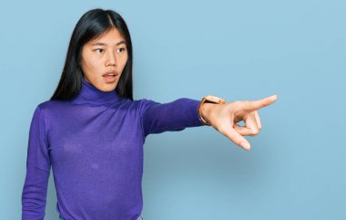 Güzel, genç Asyalı kadın gündelik giysiler giyip parmağıyla işaret ediyor. İleriyi gösteriyor, ağzı açık, şaşırmış bir ifade, ön tarafta bir şey. 