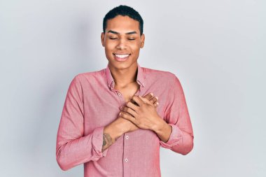 Gündelik kıyafetler giyen, göğsünde elleri kapalı, yüzünde minnet dolu jestlerle gülümseyen Afro-Amerikan bir genç. sağlık kavramı. 