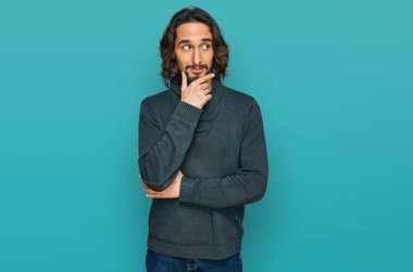 Elleri çenesinde gündelik giysiler içinde soru soran genç İspanyol bir adam, düşünceli bir ifade. Düşünceli bir yüzle gülümsüyor. şüphe kavramı. 