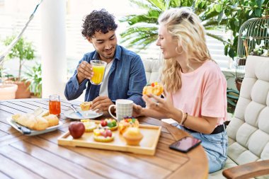 Genç çift, mutlu bir şekilde gülümsüyor. Kahvaltıyı terasta yapıyorlar..