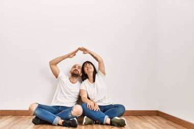 Genç İspanyol çift mutlu bir şekilde gülümsüyor. Ev sembolü yapıyorlar. Boş yeni evlerinde..