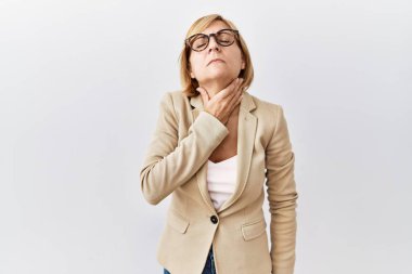 Orta yaşlı sarışın iş kadını izole edilmiş arka planda duruyor. Acı verici bir boyuna dokunuyor. Grip için boğaz ağrısı, mantar ve enfeksiyon. 