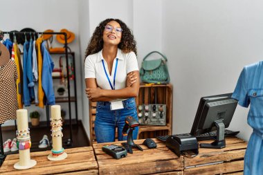 Giysi dükkanında çalışan güzel İspanyol kadın kollarını kavuşturup kameraya bakarak gülümsüyor. pozitif kişi. 