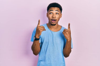 Gündelik mavi tişört giyen Afro-Amerikan genç adam şaşırmış ve şaşırmış bir şekilde yukarı baktı ve parmaklarını göstererek kollarını kaldırdı.. 