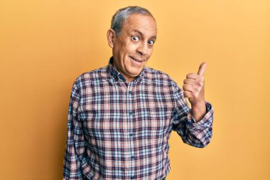 Gri saçlı, sıradan tişörtlü, mutlu yüzlü, gülümseyen ve baş parmağıyla yan tarafı gösteren yakışıklı bir son sınıf öğrencisi.. 