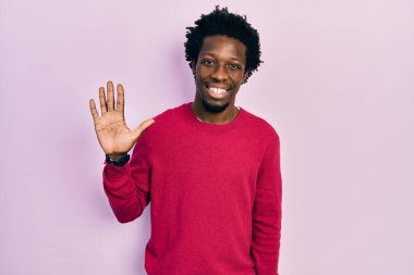 Genç Afro-Amerikalı günlük kıyafetler giymiş beş numarayı gösterip işaret ederken kendinden emin ve mutlu bir şekilde gülümsüyor.. 