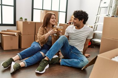 Genç çift yeni evinde kadeh kaldırırken mutlu bir şekilde gülümsüyor..