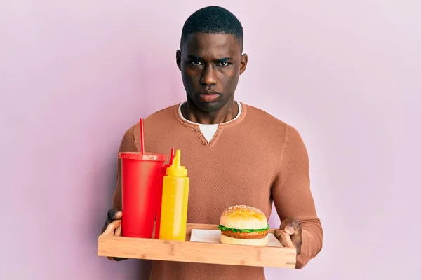 若いアフリカ系アメリカ人の男性は おいしい古典的なバーガーとソーダ懐疑的で神経を食べて 問題のために動揺を眉をひそめています 否定的な人 — ストック写真