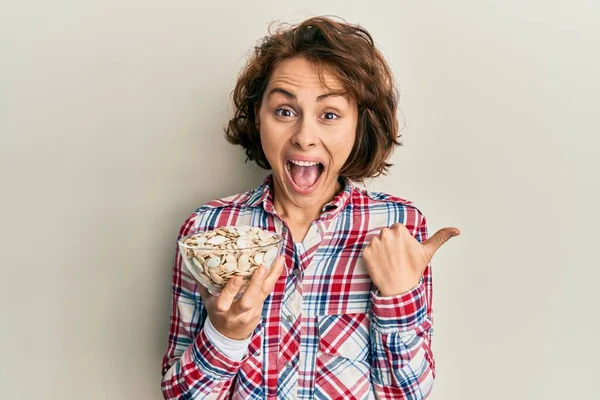 Ung Brunett Kvinna Håller Skål Med Pumpa Frön Pekar Tummen — Stockfoto