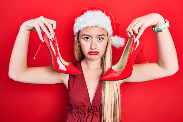 若いブロンドの女の子は 高いヒールの靴を保持クリスマスの帽子をかぶって落ち込んでおり 苦痛のために心配し 怒って恐れている 悲しい表情 — ストック写真