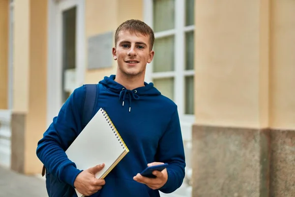 在大学里 年轻的金发学生拿着笔记本用智能手机 — 图库照片