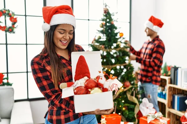 若いですラテンカップル笑顔幸せな飾るクリスマスツリーにホーム — ストック写真