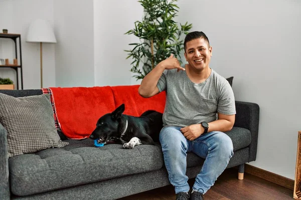 Jovem Latino Cão Sentado Sofá Casa Sorrindo Fazendo Gesto Telefone — Fotografia de Stock