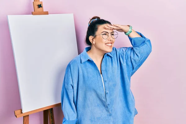 画家のイーゼルによって立って若いヒスパニック系の女性は非常に幸せと笑みを浮かべて遠くに手を頭の上に見て立っている 検索の概念 — ストック写真