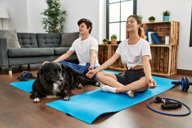 Genç beyaz çift gülümseyerek evde köpekle yoga antrenmanı yapıyor..