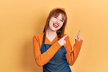 Önlük giymiş genç bir kadın gülümsüyor ve kameraya bakıyor. İki eliyle ve parmaklarıyla kenarı işaret ediyor.. 