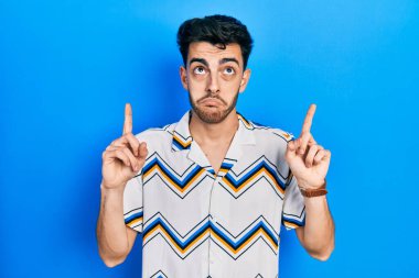 Gündelik kıyafetler giyen genç İspanyol adam üzgün ve üzgün görünüyor, parmaklarıyla yön gösteriyor, mutsuz ve depresif.. 