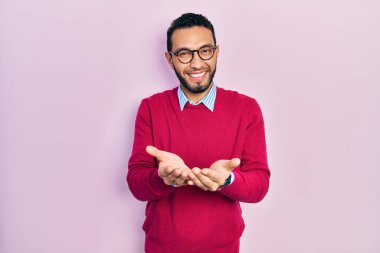 İş gömleği ve gözlük takan, elleri avuçlarında gülümseyen, el hareketi yapan İspanyol bir adam. Bekleme ve koruma 