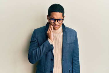 Zarif kıyafetler giyen, gözlüklü, diş ağrısı ya da diş hastalığından dolayı ağızlarına acı dolu bir ifadeyle dokunan yakışıklı İspanyol bir adam. dişçi 