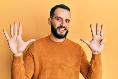 Sakallı, sıradan bir kazak giyen genç adam dokuz numarayı gösteriyor ve gülümsüyor. Kendinden emin ve mutlu.. 