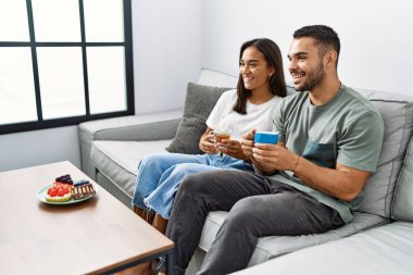 Genç latin çift evdeki kanepede kahvaltı yapıyor..