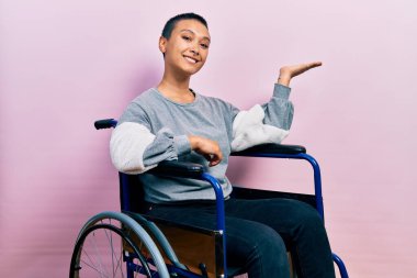 Tekerlekli sandalyede oturan, neşeli gülümseyen, elini kaldırıp kameraya bakan güzel İspanyol kadın.. 