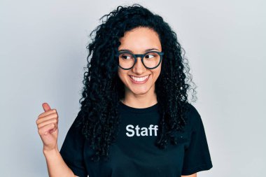 Kıvırcık saçlı, çalışkan, gülümseyen yüzüyle gülümseyen ve baş parmağıyla yüzünü gösteren İspanyol bir kadın.. 