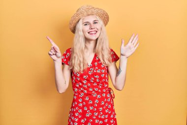 Sarışın, güzel, beyaz bir kadın. Yaz şapkası takıyor. Altıncı parmaklarıyla işaret ediyor.. 