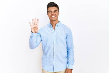 İzole edilmiş arka planda duran İspanyol gömlekli genç adam dört numarayı gösterip işaret ederken kendinden emin ve mutlu bir şekilde gülümsüyor.. 